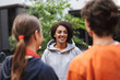 © Anton - Smiling lady with dark curly hair standing and happily talking with students in courtyard of university