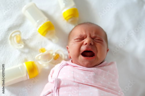 Fototapeta Crying newborn baby girl with nursing bottles. Formula drink for babies.