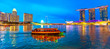 Panorama of Singapore buildings, skyscrapers and ferris wheel reflected in the sea. Tourist boat sails in the bay at evening. Singapore skyline at blue hour. Night scene waterfront marina bay.