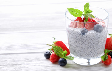 Wall Mural - Portion of chia pudding with vegan almond milk, blueberry & strawberry, mint, served in glass. Healthy vegetarian breakfast, seeds, berries, greek yogurt, wooden table. Background, close up, top view.