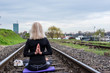 Back view of attractive senior blond woman, dressed in black, doing yoga poses outdoor on railroad. Concept: on the right path. 
