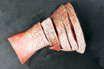 Wall Mural - Cleaned descaled sliced red snapper fish fillet pieces black marble slate background