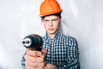 portrait of a male builder over white wall background. repair, construction, building, people and maintenance concept.The builder or the repairman holds in his hand a drill