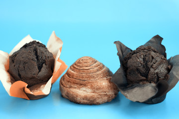 Two chocolate muffins and a cinnamon roll on a blue background close-up