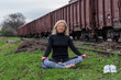 Attractive senior blond woman, dressed in black, doing yoga poses outdoor on railroad. Train in the background. Concept: on the right path.