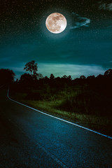 dark sky with full moon and roadway through suburban zone.