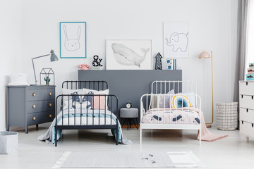 Black and white bed in siblings bedroom interior with grey cabinet and posters. Real photo