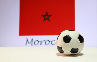 Small football on the white floor and Moroccan nation flag with the text of Morocco background. The concept of sport.