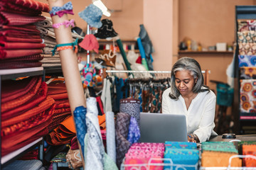 Wall Mural - Mature woman working on a laptop in her textiles shop 