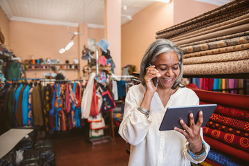 Wall Mural - Smiling fabric shop owner using a cellphone and tablet