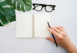 © chinnarach - close up man hand using black pencil and prepared to writing on mock up notebook in top view with tropical leaves , rubber and glasses on white table background for lifestyle concept