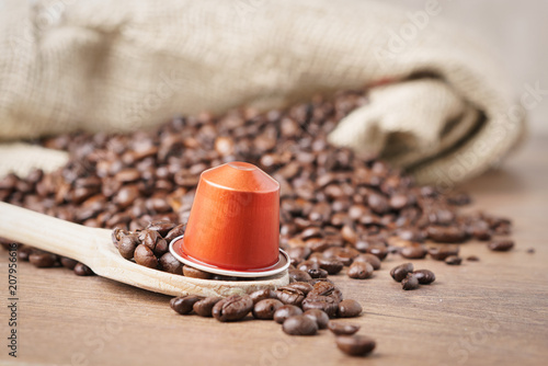 Fotografía In the foreground a coffee capsule on wooden spoon and roasted coffee beans with burlap sack on blur wooden background ,close up
