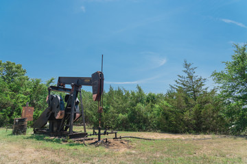 Close-up working pump jack is pumping crude oil and water emulsion at oil drilling site in rural Gainesville, Texas, US. Old pump jack and oil tanks for Energy and Industrial background.