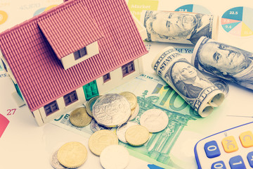 Home loan / reverse mortgage or transforming assets into cash concept : House model on pile of coins, US dollar, EU notes and a calculator, depicts a homeowner or a borrower turns properties into cash