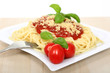 Spagetti z sosem bolońskim serem, pomidorami i zielonymi listkami bazyli.