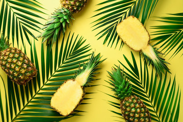  Pineapples and tropical palm leaves on pastel yellow background. Summer concept. Creative flat alay with copy space. Top view
