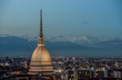 View of Turin at twilight with the illuminated Mole Antonelliana and the snow capped peaks of the Alps on the background.