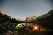 © Leander Nardin/Stocksy - couple sitting beside a campfire on a mountain lake at night with an illuminated green tent