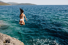 Woman Jumping In The Water From A Rocky Shore