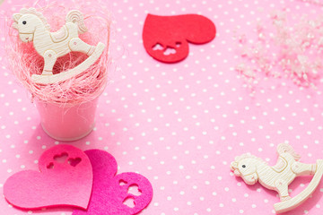 Pink baby girl theme. 2 rocking pony toys in pink small bucket and felt hearts flat lay. Top view. Copyspace