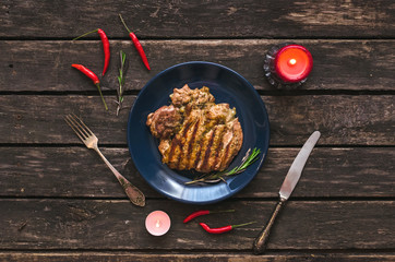 Grilled turkey meat on the blue plate with red chili peppers around and two burning candles the wooden background.