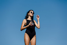 Portrait Of Attractive Woman In Black Bikini Drinking Juice On The Rocky Shore