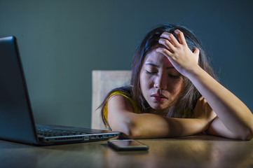 dramatic portrait scared and stressed Asian Korean teen girl or young woman with laptop computer and mobile phone suffering cyber bullying stalked