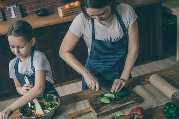 Poster - Woman standing and cooking vegetables while daughter mixing salad in the bowl.