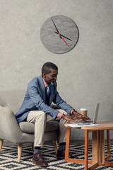 Wall Mural - stylish middle aged african american businessman using laptop at table with coffee and newspaper