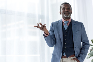 Wall Mural - thoughtful african american businessman in blue jacket gesturing near window