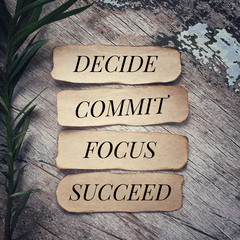 motivational and inspirational quote - ‘decide, commit, focus, succeed’ written on pieces of papers.