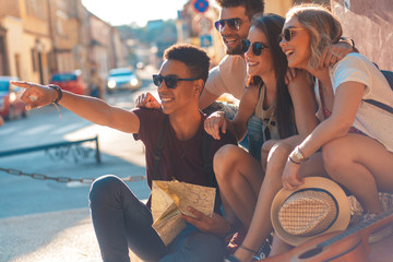 Group of friends on vacation with map walking through the city and having good time.