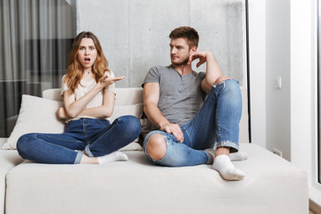 Sticker - Displeased young loving couple sitting on sofa quarrel.