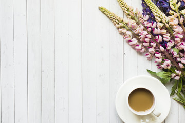 Still life with a Cup of coffee and lupine flowers donut on a light wooden table. Copy space