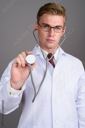 Young Handsome Man Doctor With Blond Hair Against Gray Backgroun