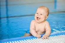 Happy, Smiling Little Baby Boy On Edge Of Blue Swimming Pool In Water.