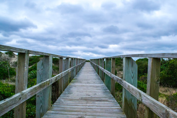  Endless beach walk, wooden plank walkway focused on a distance vantage point, ominous stormy clouds disappearing into horizon - located in Oak Island North Carolina, cloudy day