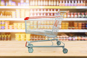 Supermarket with product shelves blur background with empty shopping cart on wood table