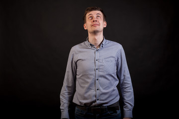 Wall Mural - A dark haired white man looking up and smile in a plaid shirt and jeans on a black isolated background