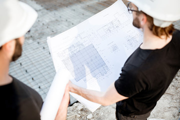 Two builders working with architectural drawings standing on the construction site outdoors