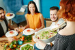 © pressmaster - Back view of crop woman bringing to table white dish with pasta while eating with friends.