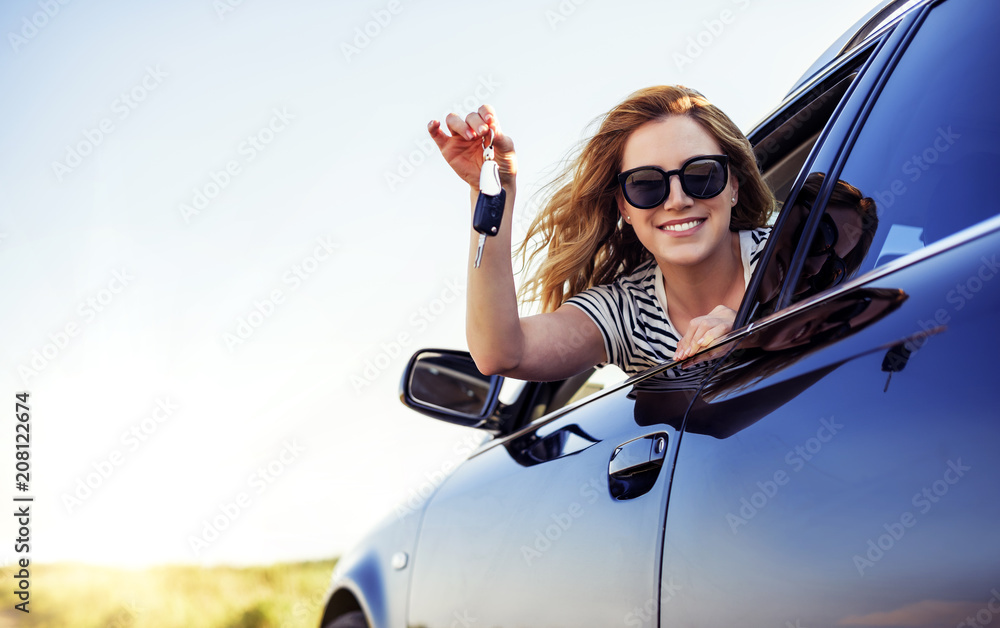 An attractive woman in a car holds a car key in her hand. - obrazy, fototapety, plakaty 