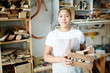 © pressmaster - Adult woman in apron holding wooden box with tools and looking at camera while standing in carpenter workshop.