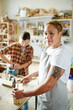 © pressmaster - Female woodworker looking at camera while driving nails into nice lumber box in workshop.
