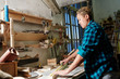 © pressmaster - Side view of female woodworker standing near workbench and measuring lumber plank while working in workshop.