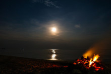 Long Exposure Of A Full Moon With Bonfire On A Sandy Beach And Ocean In The Background, Khanom Beach, Thailand