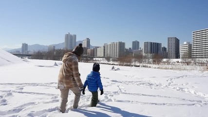 Wall Mural - Asian mother and her son playing snow together in the park , sapporo japan slow motion 