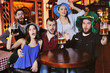 © Evgeniy Kalinovskiy - group or company of friends - young guys and girls holding glasses of beer, watching football, laughing and smiling at the bar during the Oktoberfest festival