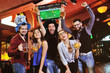 © Evgeniy Kalinovskiy - group or company of friends - young guys and girls holding glasses of beer, watching football, laughing and smiling at the bar during the Oktoberfest festival