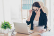© deagreez - Portrait of smart agent successful business shark trendy woman looking out glasses at screen of laptop holding tablet in hand sitting in modern office with interior
